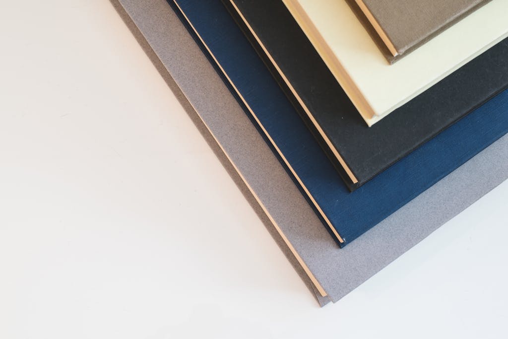 A stack of minimalist hardcover books in varied colors, viewed from above.
